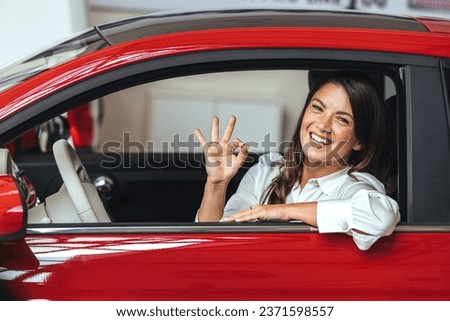 Happy woman driving a car with thumbs up. Beautiful girl looking through the car window and showing ok. Business woman through the car window showing ok