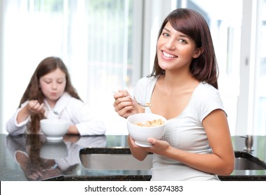 Happy woman eating breakfast cereal with daughter