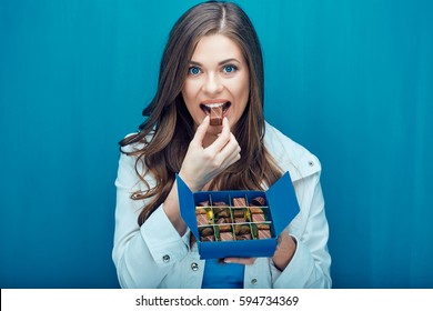 Happy Woman Eating Chocolate Candy. Portrait On Blue Background.