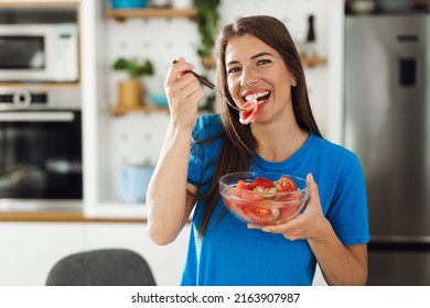 Happy Woman Eating A Salad In The Kitchen And Looking At Camera.