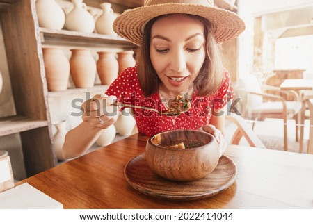 Happy woman eats kharcho soup from Georgian cuisine or Hungarian meat goulash in a rustic restaurant.