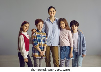 Happy Woman Embracing Group Of Kids. Studio Portrait Of Smiling School Teacher And Students Looking At Camera. Group Of Children Together With Tutor At Educational Center Or Counselor In Day City Camp