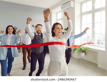 Happy woman employee running to the red ribbon with raised arms celebrating crossing finishing line in office with people colleagues in background. Business competition and teamwork concept. - Powered by Shutterstock