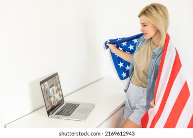 Happy woman employee sitting wrapped in USA flag, shouting for joy in office workplace, celebrating labor day or US Independence day. Indoor studio studio shot isolated on yellow background