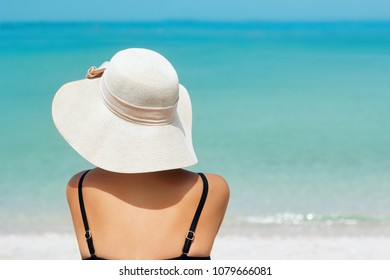 Happy Woman Enjoying Beach Relaxing Joyful In Summer By Tropical Blue Water. Beautiful Bikini Model Happy On Travel Wearing Beach Sun Hat On Beach. Girl On A Tropical Beach With Hat
