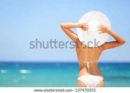 Happy woman enjoying beach relaxing joyful in summer by tropical blue water. Beautiful bikini model happy on travel wearing beach sun hat on Hapuna beach, Big Island, Hawaii, USA.
