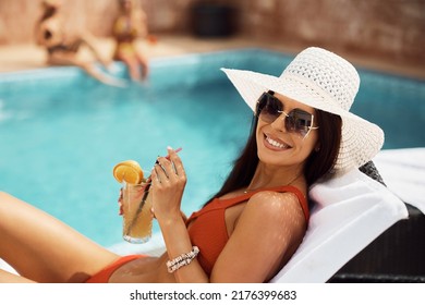 Happy Woman Enjoying In Cocktail While Relaxing On Deck Chair On Summer Day By Swimming Pool. 