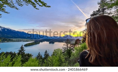 Happy woman enjoying the panoramic sunset view on Lake Faak from Taborhoehe in Carinthia, Austria, Europe. Austrian Alps. Water surface reflecting soft sunlight. Remote alpine landscape in summer