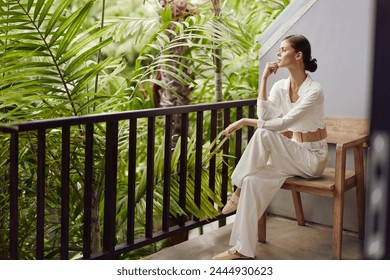 Happy Woman Enjoying Tropical Vacation on a Balcony Terrace, Smiling Under the Sunlight with Trendy Sunglasses A Young Girl Resting and Relaxing in a Stylish Apartment with a Beautiful View of the - Powered by Shutterstock