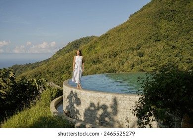 Happy woman enjoying  tropical vacation near infinity pool with a jungle  sea view in  Bali. Young woman enjoying the sun at infinity summer swimming pool at luxurious resort - Powered by Shutterstock