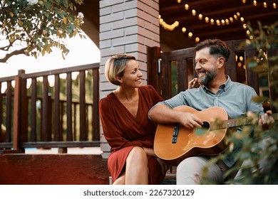 Happy woman enjoying while her husband is playing acoustic guitar for her in the backyard. Copy space. - Powered by Shutterstock