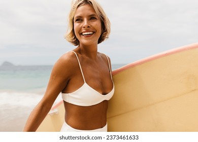 Happy woman enjoys a solo beach vacation, embracing a healthy lifestyle filed with beach activities. Female surfer smiling confidently as she walks to the best surfing spots with her surfboard. - Powered by Shutterstock