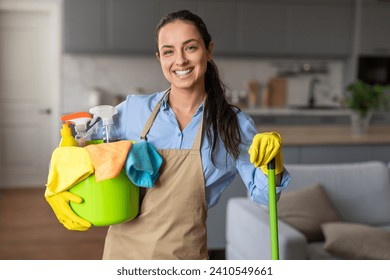 Happy woman equipped with mop and bucket full of cleaning supplies flashes warm smile, ready to tackle household chores with confidence - Powered by Shutterstock