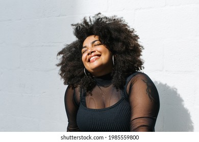 Happy woman in fashionable wear standing near wall. Pretty female in black outfit on white background.