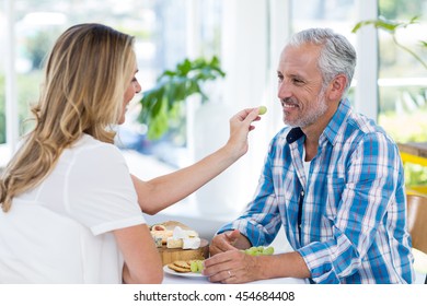 Happy woman feeding grapes to husband in restaurant