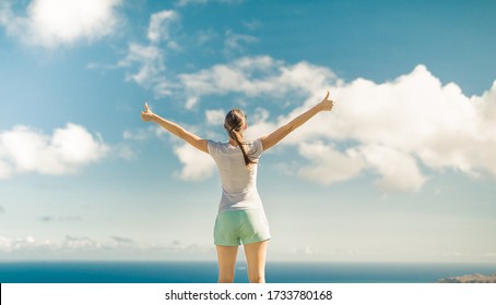 Happy woman feeling free with her thumbs up against blue sunny sky. People happiness, and feeling inspired concept. 