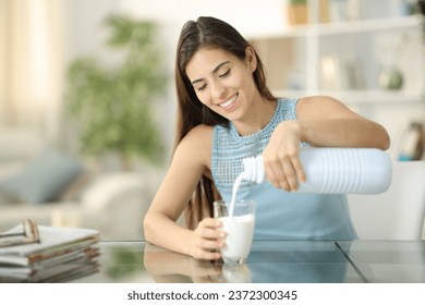 Happy woman filling glass with milk sitting at home - Powered by Shutterstock