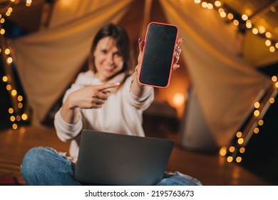 Happy Woman Freelancer Showing Phone While Working Laptop On Cozy Glamping Tent In Summer Night. Luxury Camping Tent For Outdoor Holiday And Vacation. Lifestyle Concept