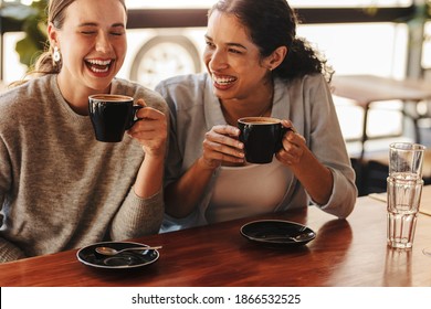 Happy woman friends in a cafe having coffee. Two females sitting at a coffee table talking and laughing.