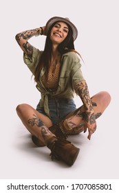 Happy Woman Full Body Portrait With Tattoo And Hat Sit On The Floor Against White Wall Background. Filtered Image.