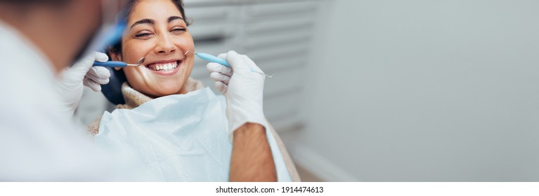 Happy woman getting dental checkup at dentistry. Dentist using dental equipment for examination of teeth of a female patient.