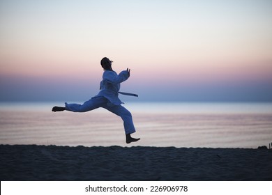Happy woman in gi jumping on the sunset beach