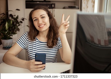 A happy woman girl works remotely from home and communicates via video call with friends and relatives in her office. Distance learning and work online. Using a mobile phone and computer. - Shutterstock ID 1711337323