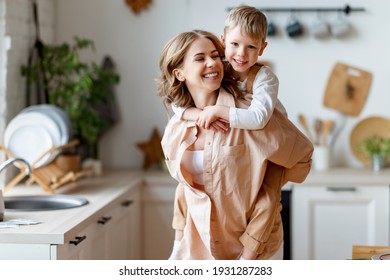 Happy woman giving piggyback ride to cheerful boy while playing in kitchen at home together - Powered by Shutterstock