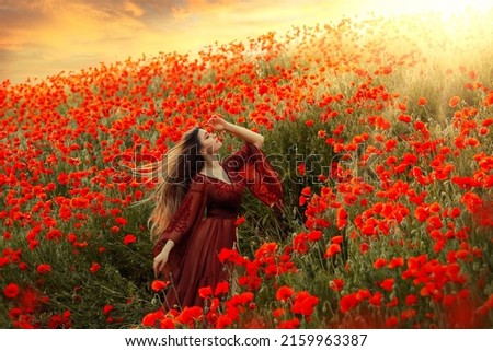 happy woman goddess walks in poppy field long hair flying in wind. Girl princess enjoys summer nature, red poppies flowers green grass, sun light shining, dramatic sky, sunset. vintage silk dress.