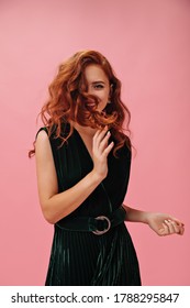 Happy Woman In Green Outfit Plays Hair On Pink Background. Charming Red Haired Lady In Dark Stylish Dress Has Fun On Isolated Backdrop..