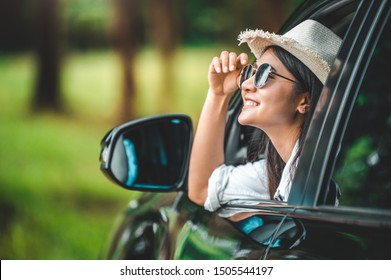 Happy woman hand holding hat outside open window car with green forest woods mountain background. People lifestyle relaxing as traveler on road trip in holiday vacation. Transportation and travel