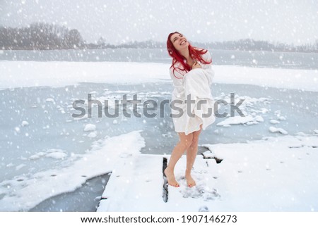Happy woman hardening and winter swimming concept. Barefoot female enjoying cold snowy weather on an icy lake, mood-lifting and immune system boosting outdoor activities in the wintry landscape.
