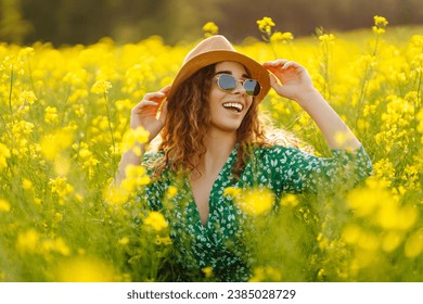 A happy woman in a hat walks through a blooming rapeseed field. Beautiful woman posing in a rapeseed field on a sunny day. Concept of nature, relaxation. - Powered by Shutterstock