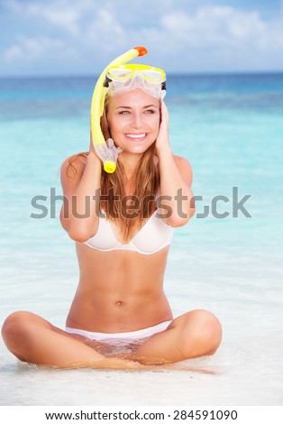 Happy woman having fun on the beach, sitting on beautiful sandy coast wearing snorkeling outfit, active summer vacation