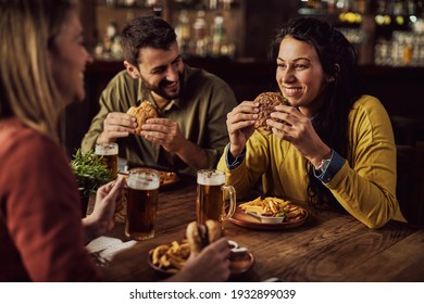 Happy woman having fun while talking to her friends and eating hamburger in a pub. 