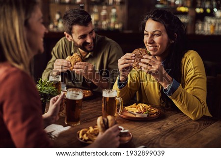 Happy woman having fun while talking to her friends and eating hamburger in a pub. 