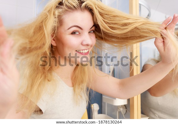 Happy woman having long blonde hair. Positive female\
after taking a shower feeling clean showing condition of her hairdo\
with joy