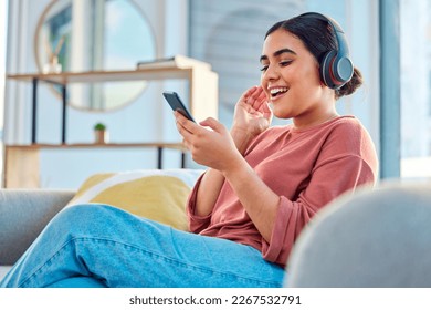 Happy woman, headphones and smartphone in living room on social media app, audiobook or radio podcast on sofa. Young girl, mobile music and listening to audio, streaming and singing in home lounge - Powered by Shutterstock