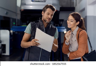 Happy Woman And Her Auto Mechanic Reading Report Of A Car Repair In A Workshop.