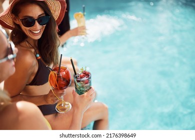 Happy woman and her female friends toasting with summer cocktails and having fun at swimming pool. Copy space.