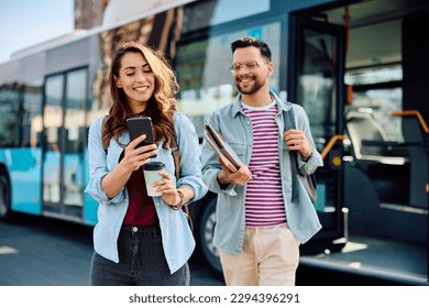 Happy woman and her friend using app on smart phone while arriving at city bus station.
