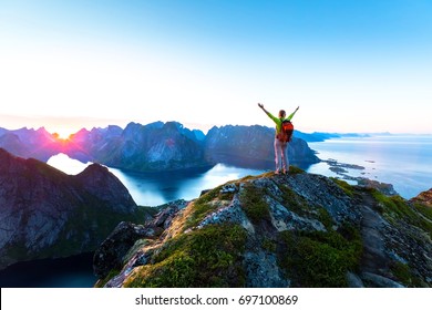 Happy woman hiker enjoying scenic view of midnight sun at the top of Reinebringen hike above Reine village in the Lofoten archipelago during arctic summer, Norway - Powered by Shutterstock