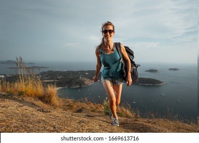 Happy woman hiker walks up the hill towards the camera with tropical islands on the background