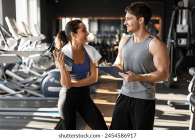 Happy woman holding bottle with water and talking to her male trainer after workout at gym - Powered by Shutterstock