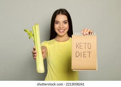 Happy Woman Holding Celery And Notebook With Words Keto Diet Against Light Grey Background, Focus On Hands