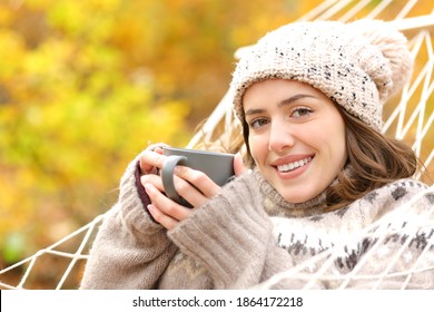 Happy woman holding coffee cup lying on hammock looking at camera in autumn holiday - Shutterstock ID 1864172218