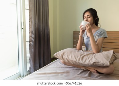 Happy woman holding and drinking coffee on the bed in the morning.