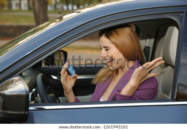 Happy woman holding\
driving license in car