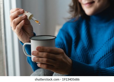 Happy Woman Holding A Dropper Of Cbd Cannabis Hemp Oil In Tea Cup - Focus On Dropper