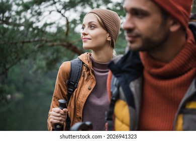 Happy Woman Holding Hiking Stick Near Boyfriend On Blurred Foreground